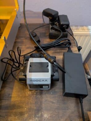 TOCOAA Air Assist pump with cables on a table, with the laser's power supply unit next to it.