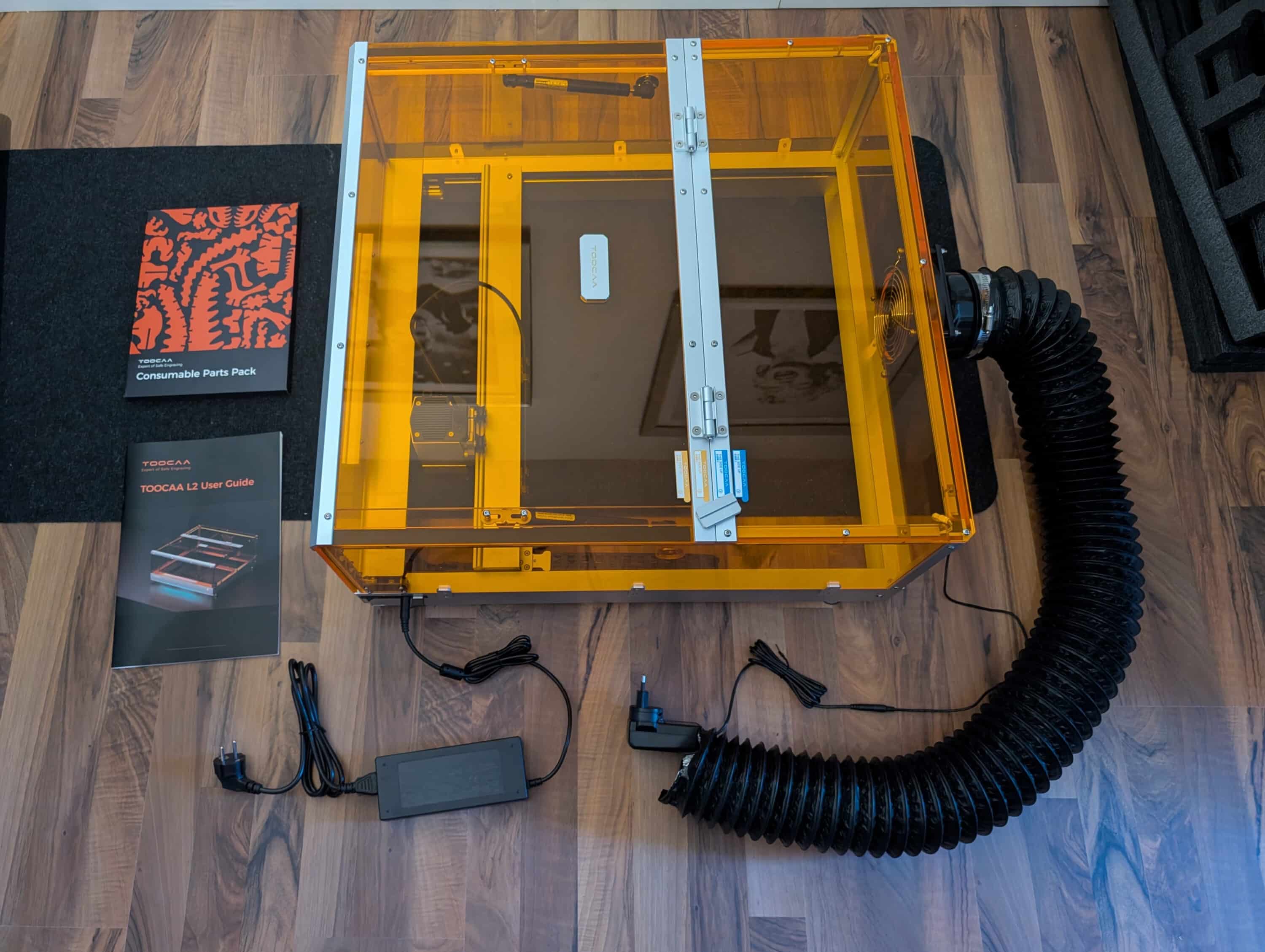 Fully assembled Toocaa L2 laser engraver with closed housing, connected extraction system and accessories laid out