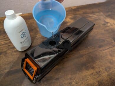 Measuring cup with water is filled into the open fresh water tank of the UWANT D100, cleaning solution next to it.